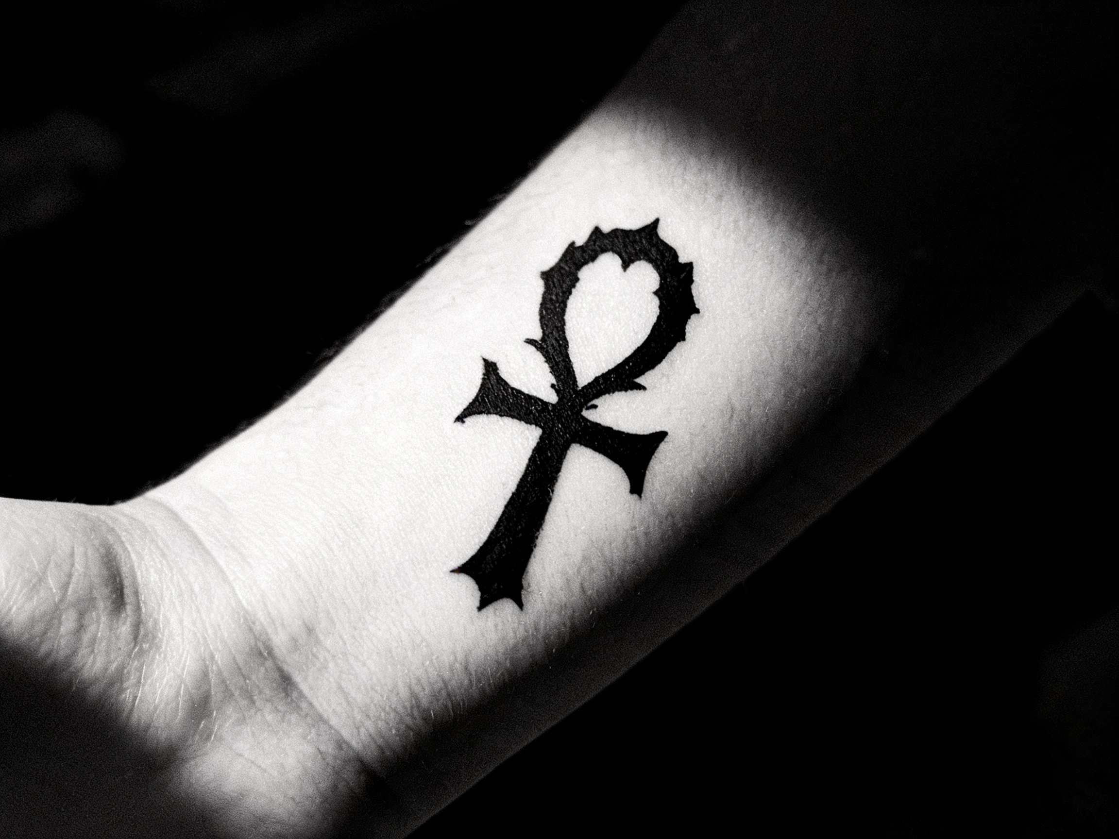 Dettaglio tatuaggio blackwork gotico con croce ansata e ornamenti dark su pelle, fotografia noir ad alto contrasto