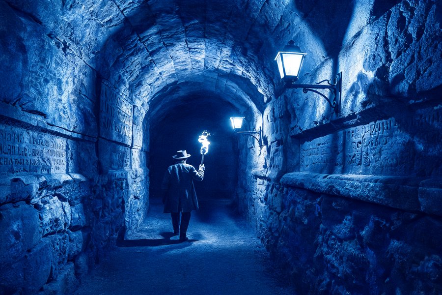 Tunnel del labirinto sotterraneo di Parigi: gallerie nella pietra calcarea illuminate da una lanterna con figure che scompaiono nell'oscurità, cianotipo