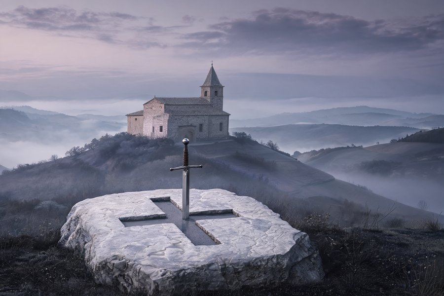 Spada medievale conficcata nella roccia a forma di croce sul colle di Montesiepi al tramonto nella nebbia toscana, stile Friedrich